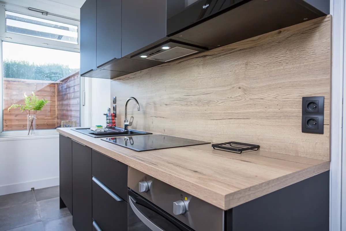 Maison La Vesée, l'appartement Heliconia, la cuisine, meubles noirs côté évier, vue de côté avec fenêtre en arrière-plan