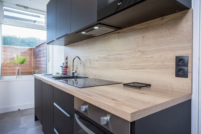 Maison La Vesée, l'appartement Heliconia, la cuisine, meubles noirs côté évier, vue de côté avec fenêtre en arrière-plan