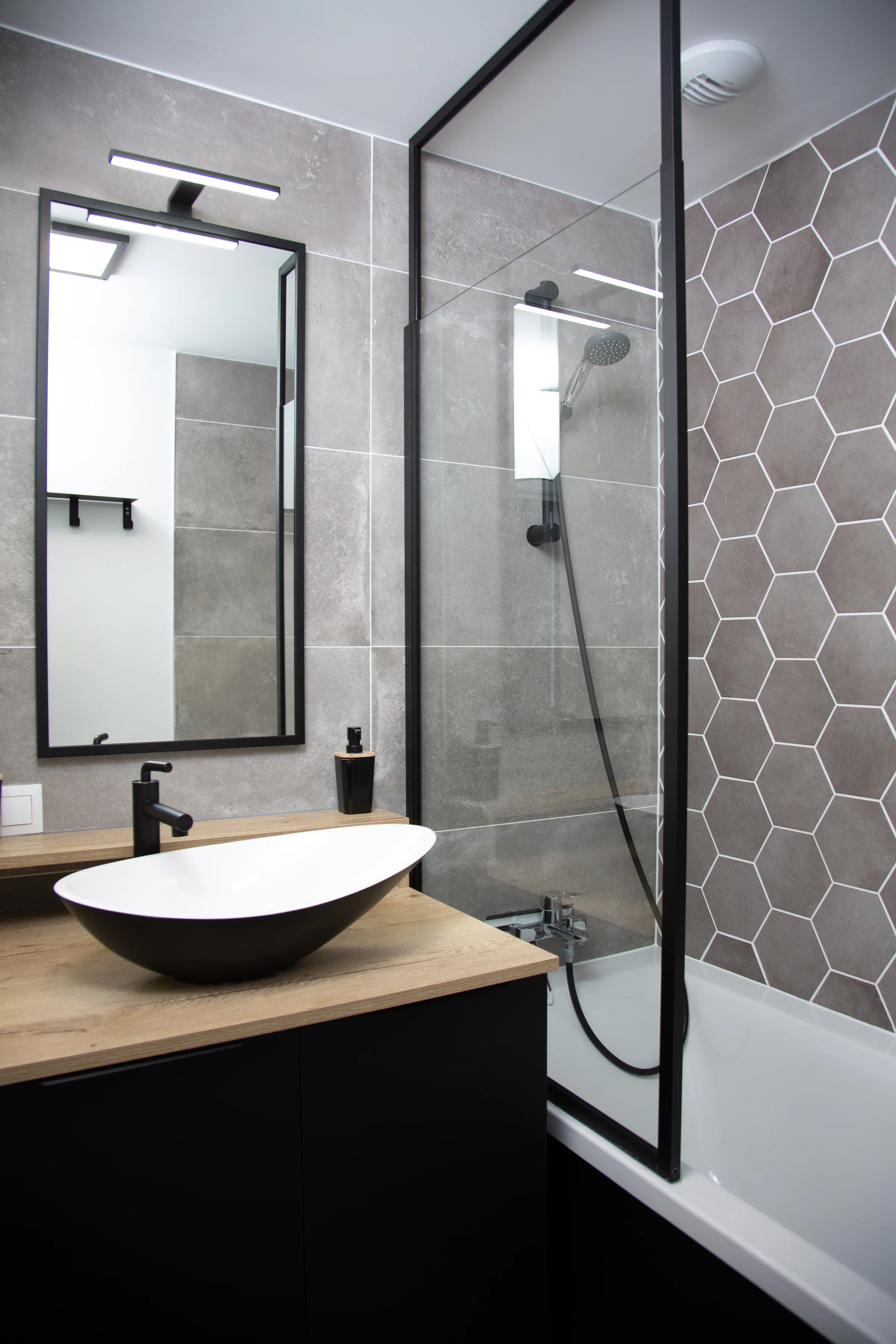 Maison La Vesée, l'appartement Heliconia, la salle de bain du rez-de-chaussée, vue d'ensemble sur le meuble vasque et la baignoire avec espace douche, carrelage gris au mur