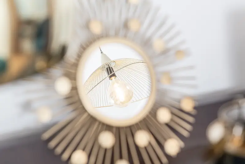 Maison La Vesée, l'appartement Heliconia, la suite parentale, détail miroir soleil or réfléchissant le luminaire de la chambre