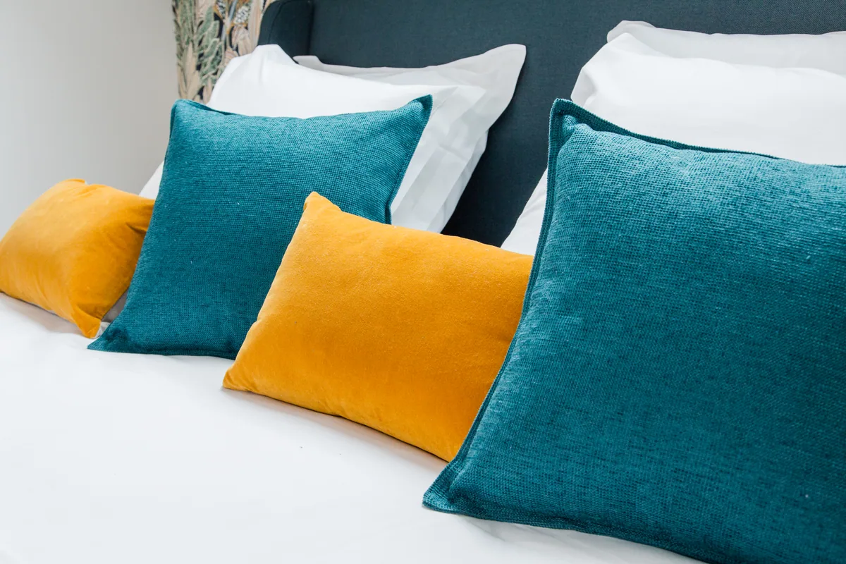 Maison La Vesée, l'appartement Heliconia, la suite parentale, détail décoration coussins bleus et jaunes sur le lit