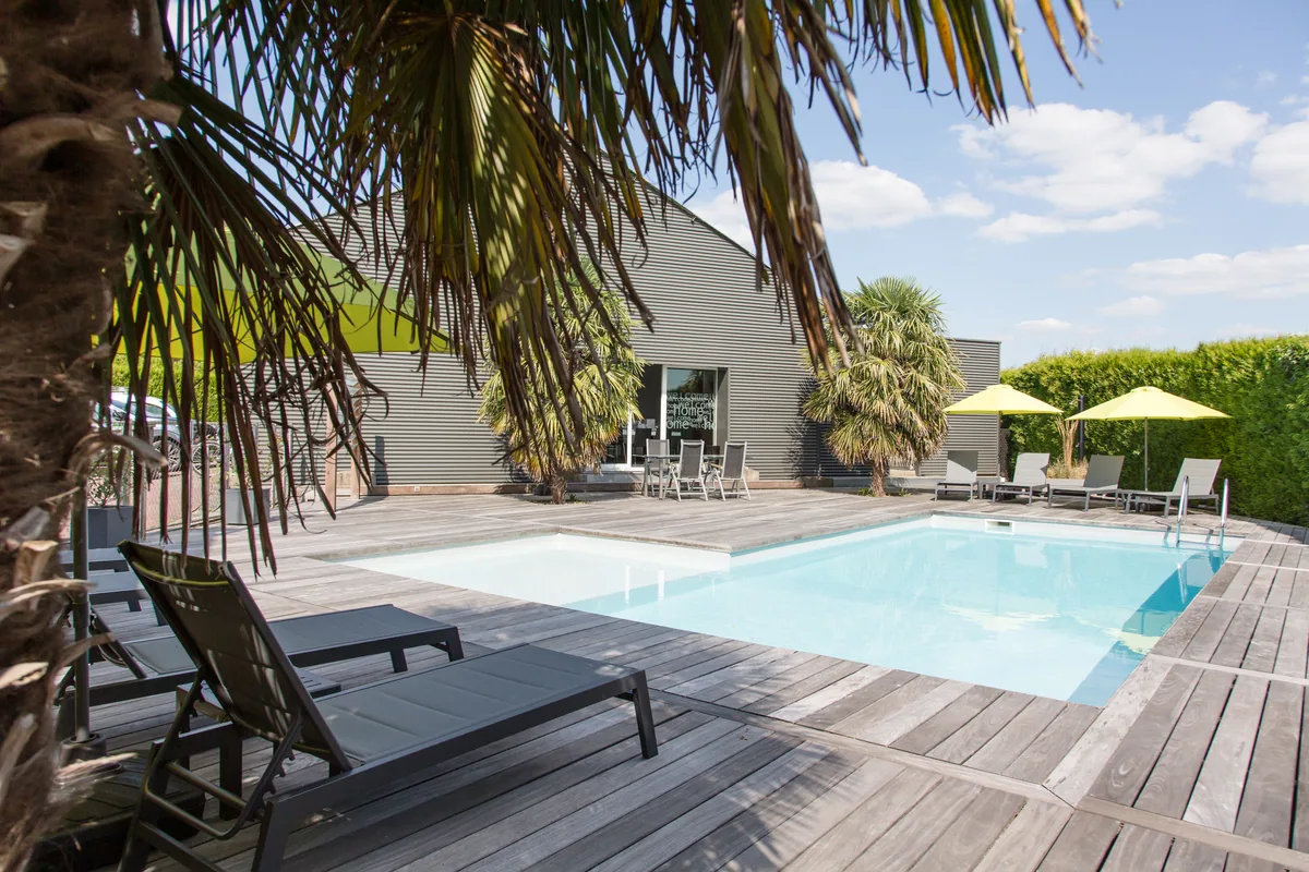 La piscine de Maison La Vesée, vue sur le bassin avec les feuilles de palmier en premier plan