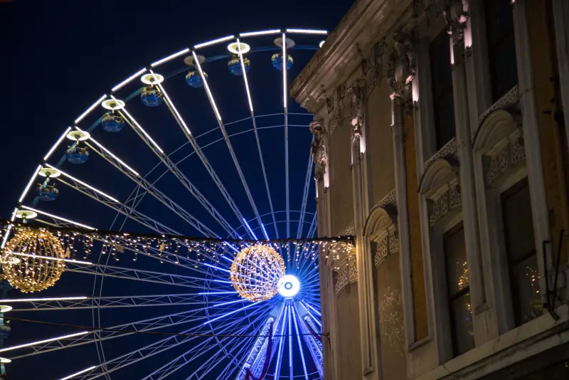 Das Riesenrad in blauem Licht bei Einbruch der Dunkelheit, neben einer historischen Fassade der Grand'Place