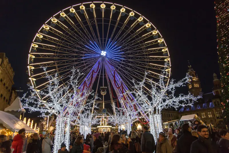 Das beleuchtete Riesenrad am Ende einer Allee aus Lichterbäumen, auf der dicht gefüllten Grand'Place