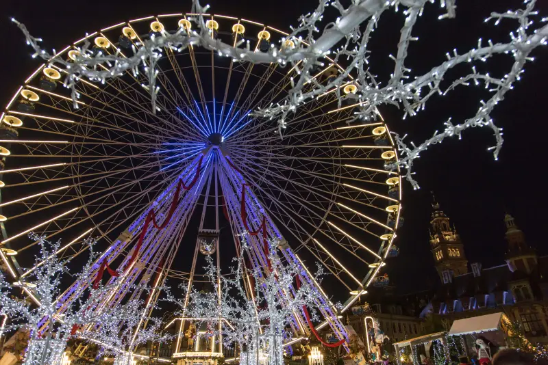 Das Riesenrad, eingerahmt von den Zweigen eines Lichterbaums, über den Holzhäuschen